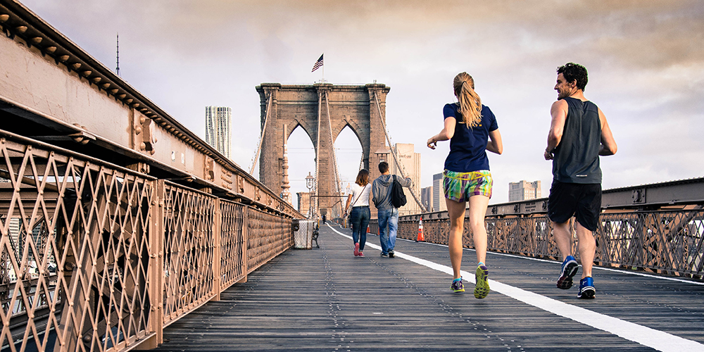 Woman and man jog across a bridge as two people walk ahead of them