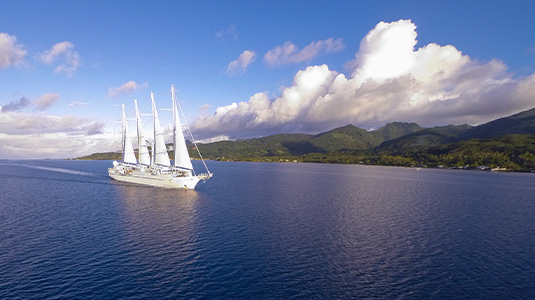 Sail boat with four masts sailing by green coast