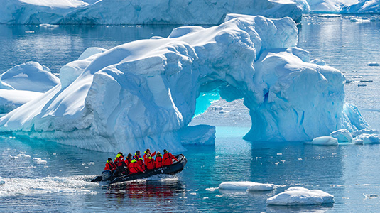 Small boat exploring blue icebergs floating in ocean